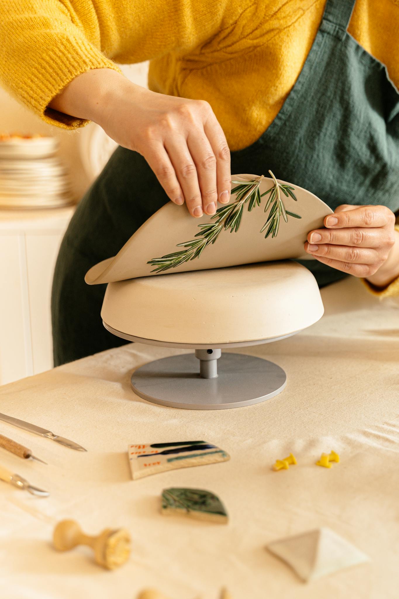 Close-up of an artisan applying rosemary imprint to pottery in a warm, creative setting.